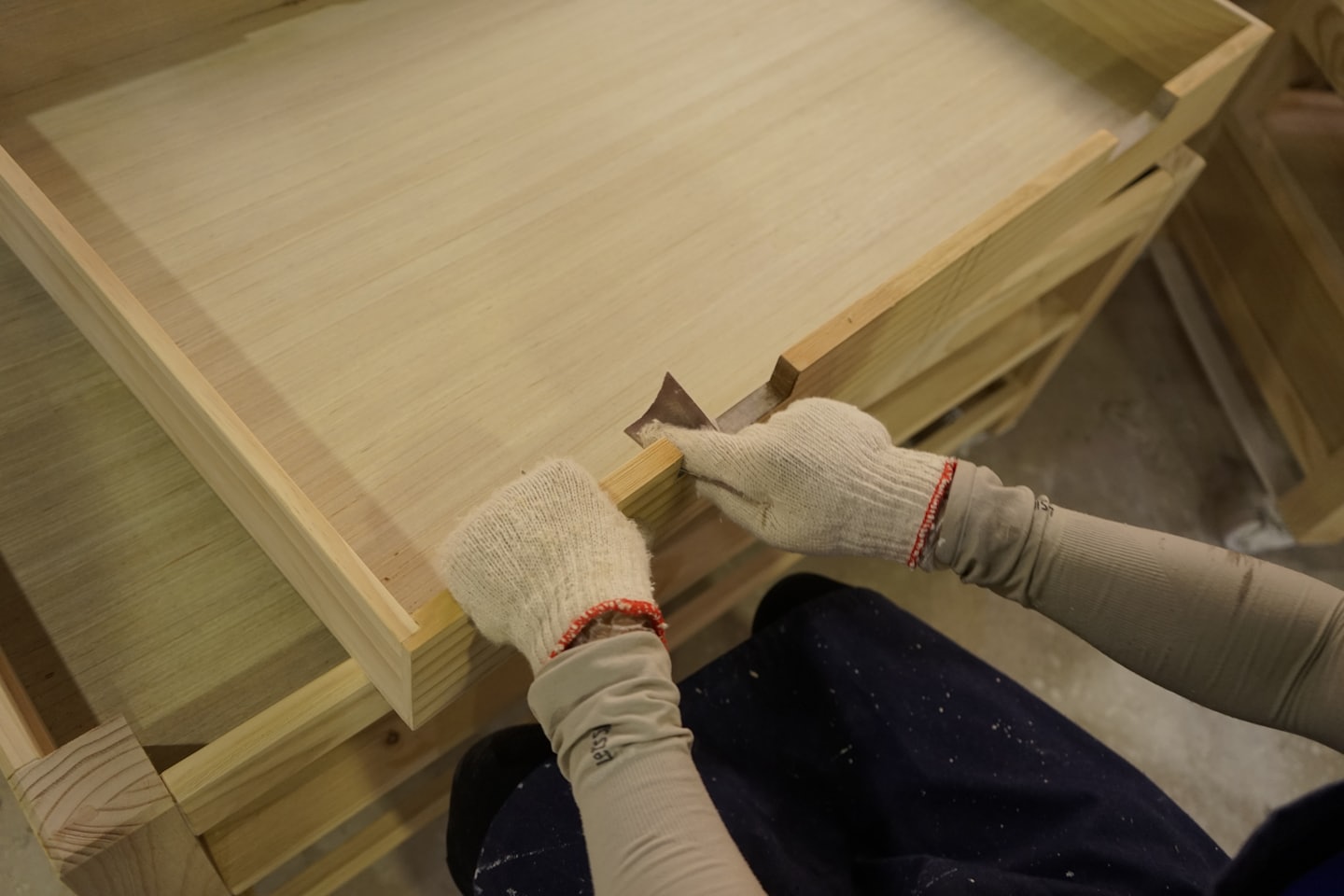 Handskar på händerna slipar en träyta i en verkstad.