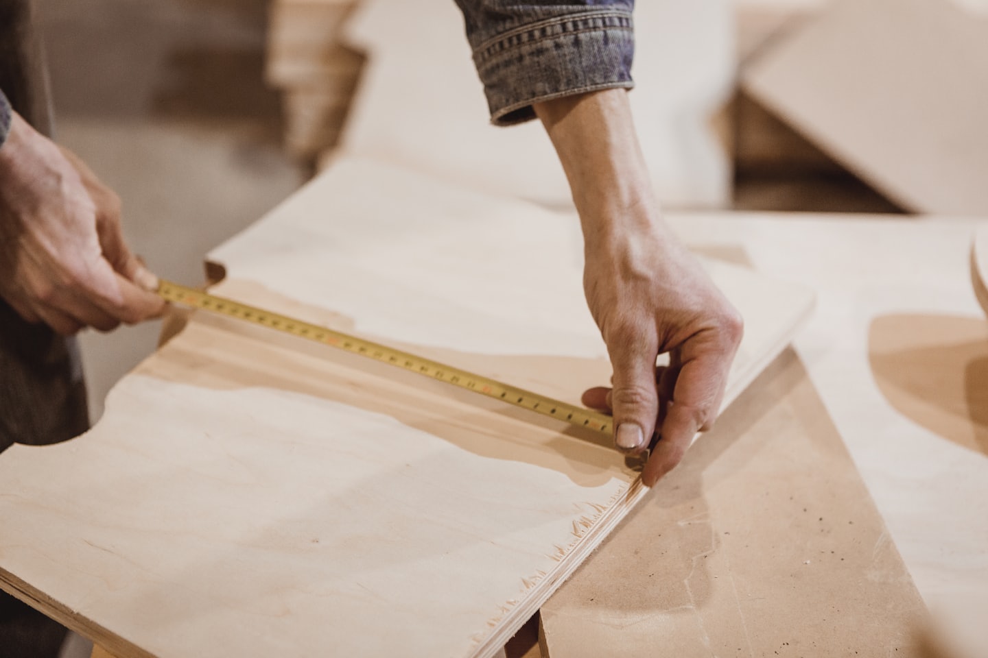 Händer mäter plywood med ett gult måttband.